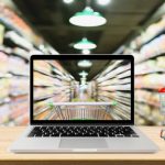 supermarket aisle blurred background with laptop computer and cart on wood table online shopping concept