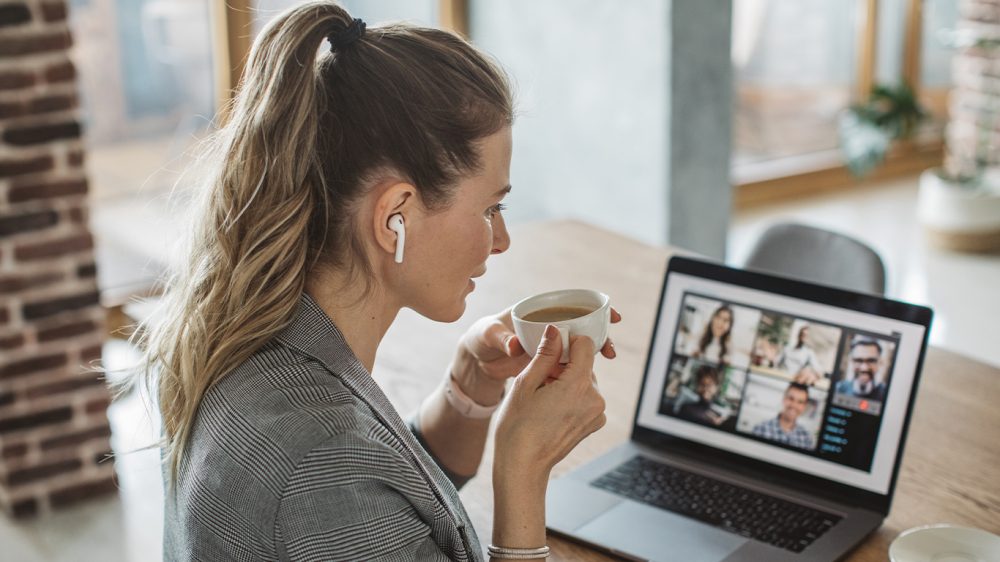 Frau sitzt zu Hause am Laptop und tirnkt einen Cafe