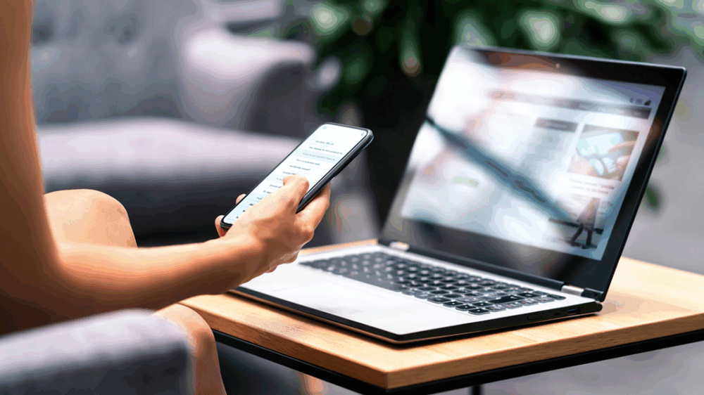 Frau mit Smartphone und modernem Notebook PC Computer auf dem Tisch schaut sich eine Website an.
