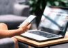 Frau mit Smartphone und modernem Notebook PC Computer auf dem Tisch schaut sich eine Website an.