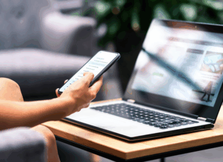 Frau mit Smartphone und modernem Notebook PC Computer auf dem Tisch schaut sich eine Website an.