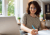 Junge Frau sitzt am Tisch mit Laptop und betreibt E-Learning.