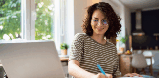Junge Frau sitzt am Tisch mit Laptop und betreibt E-Learning.