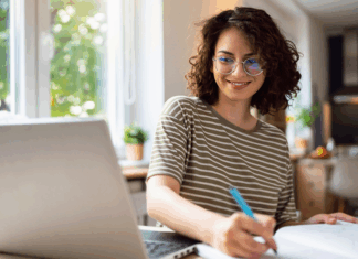 Junge Frau sitzt am Tisch mit Laptop und betreibt E-Learning.