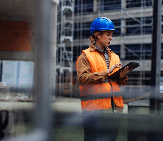 Junge Arbeiterin mit ihrem digitalen Tablet auf einer Baustelle