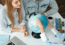 Junge Menschen in einem Reisebüro mit einem Reisebüro, das das Reiseziel auf einem Globus wählt und neugierig aussieht und lächelt.