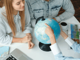 Junge Menschen in einem Reisebüro mit einem Reisebüro, das das Reiseziel auf einem Globus wählt und neugierig aussieht und lächelt.