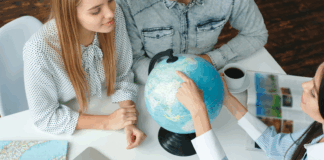 Junge Menschen in einem Reisebüro mit einem Reisebüro, das das Reiseziel auf einem Globus wählt und neugierig aussieht und lächelt.