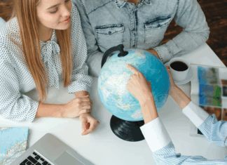 Junge Menschen in einem Reisebüro mit einem Reisebüro, das das Reiseziel auf einem Globus wählt und neugierig aussieht und lächelt.