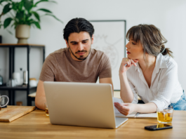 Symbolbild für Artikel: Warum der Weg zum Eigenheim so kompliziert geworden ist; Mann und Frau besprechen etwas und sitzen am Laptop