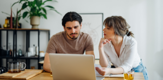 Symbolbild für Artikel: Warum der Weg zum Eigenheim so kompliziert geworden ist; Mann und Frau besprechen etwas und sitzen am Laptop