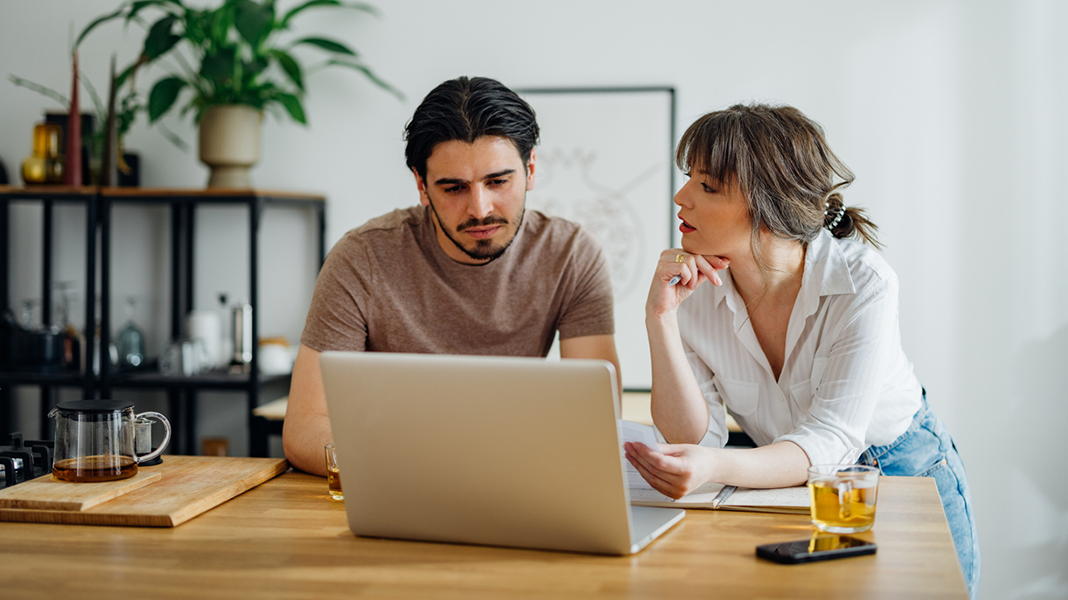 Header_techtag_meinhaus.digital und HYPOFY Symbolbild für Artikel: Warum der Weg zum Eigenheim so kompliziert geworden ist; Mann und Frau besprechen etwas und sitzen am Laptop