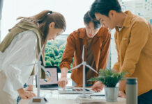 Symbolbild zu Energiewende, 3 Personen stehen um einen Tisch mit Windrädern und planen ein Projekt.