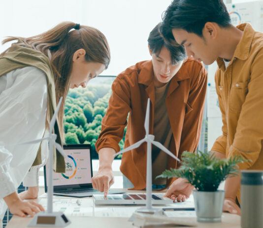 Symbolbild zu Energiewende, 3 Personen stehen um einen Tisch mit Windrädern und planen ein Projekt.