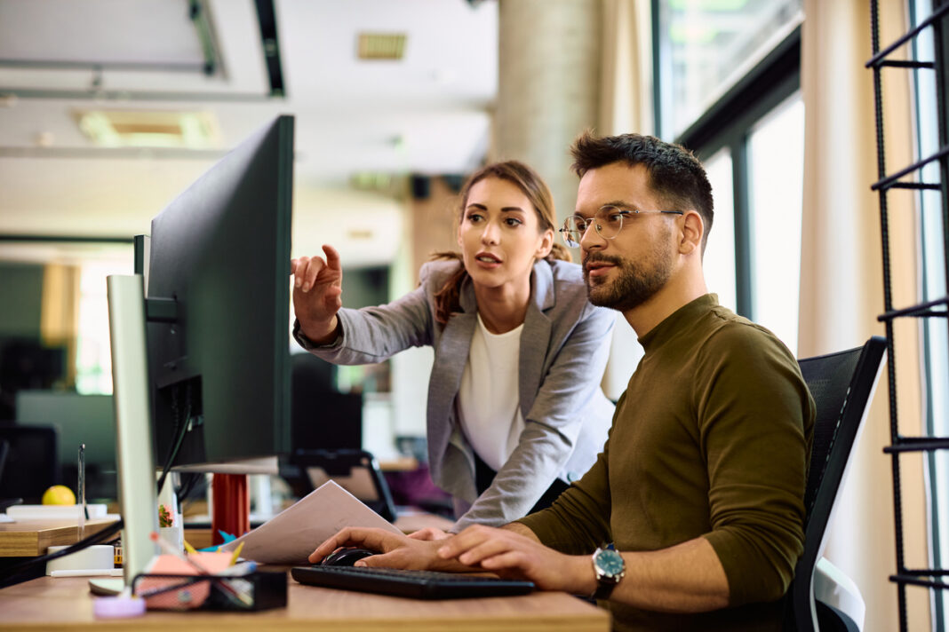 Junge Kolleginnen und Kollegen kooperieren bei der Arbeit am Computer im Büro.