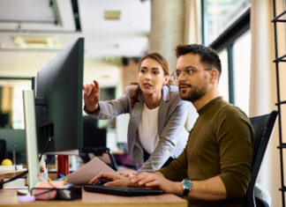 Die nächste KI-Revolution arbeitet unsichtbar Junge Kolleginnen und Kollegen kooperieren bei der Arbeit am Computer im Büro.