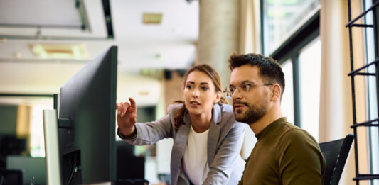 Junge Kolleginnen und Kollegen kooperieren bei der Arbeit am Computer im Büro.