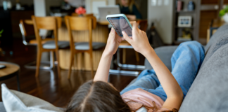 Teenager-Mädchen zu Hause, das sich soziale Medien auf ihrem Handy anschaut