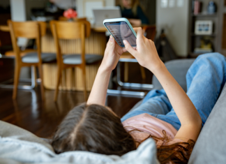 Teenager-Mädchen zu Hause, das sich soziale Medien auf ihrem Handy anschaut