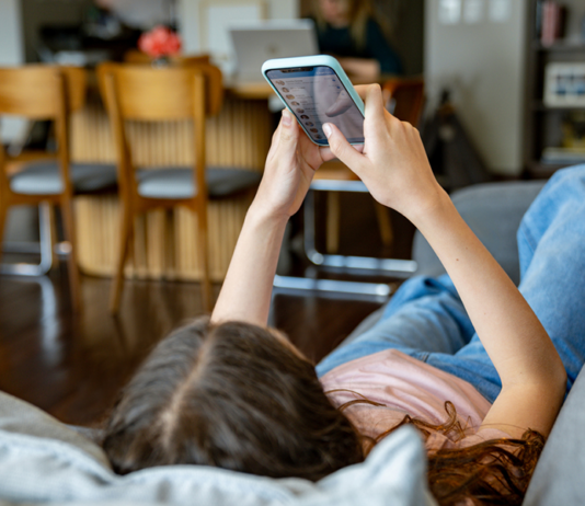 Teenager-Mädchen zu Hause, das sich soziale Medien auf ihrem Handy anschaut