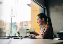 Lächelnde Frau, die aus der Ferne am Laptop arbeitet, während sie im Café Kaffee trinkt