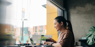 Lächelnde Frau, die aus der Ferne am Laptop arbeitet, während sie im Café Kaffee trinkt