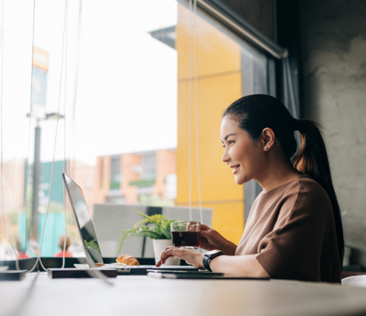 Lächelnde Frau, die aus der Ferne am Laptop arbeitet, während sie im Café Kaffee trinkt
